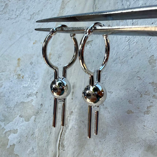 Silver earrings with a spherical design held by tweezers on a textured surface