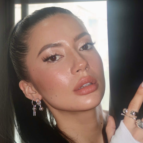 Close-up of a woman with makeup and jewelry, wearing silver stud earrings and rings.