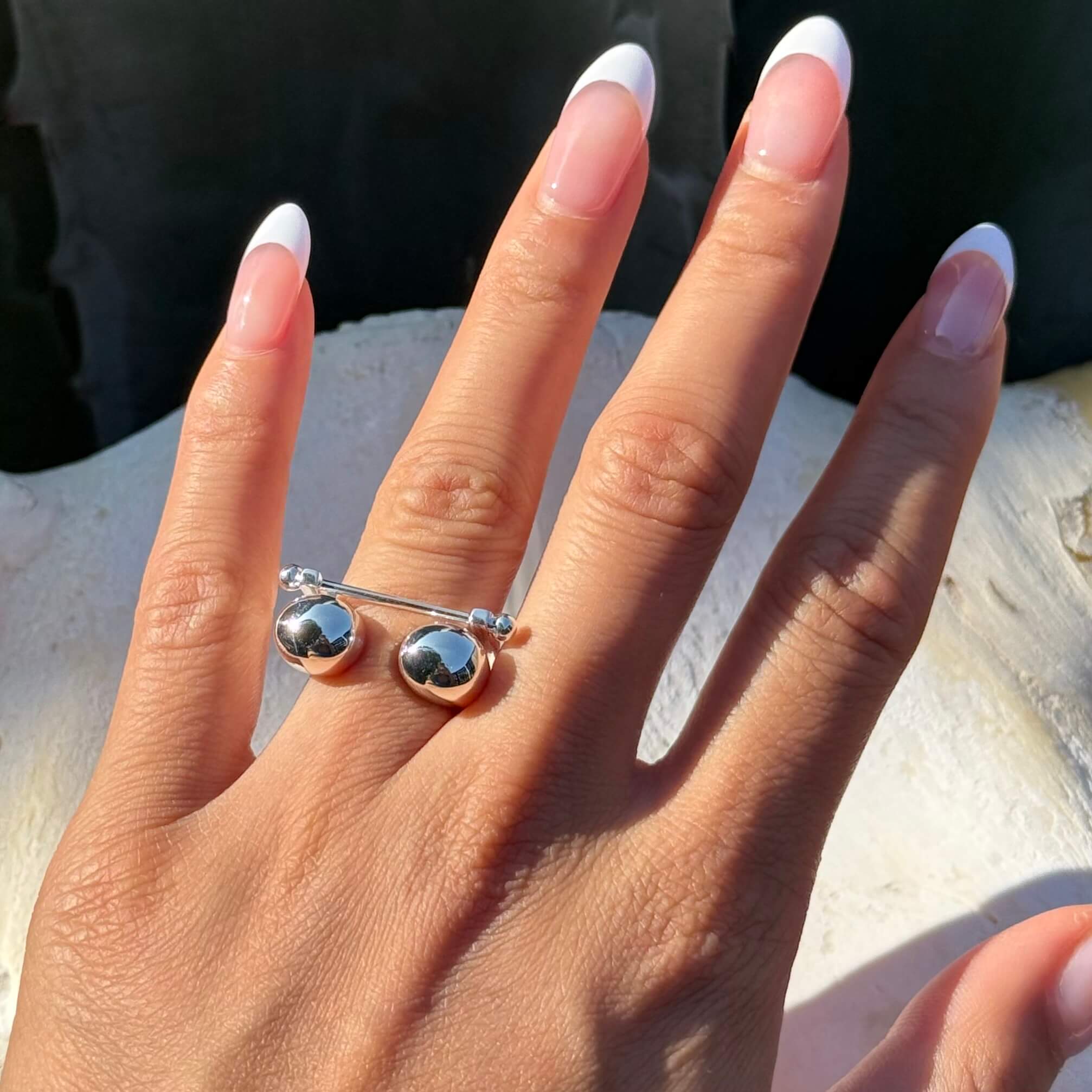 Hand wearing bacll stackable silver ring on a light background