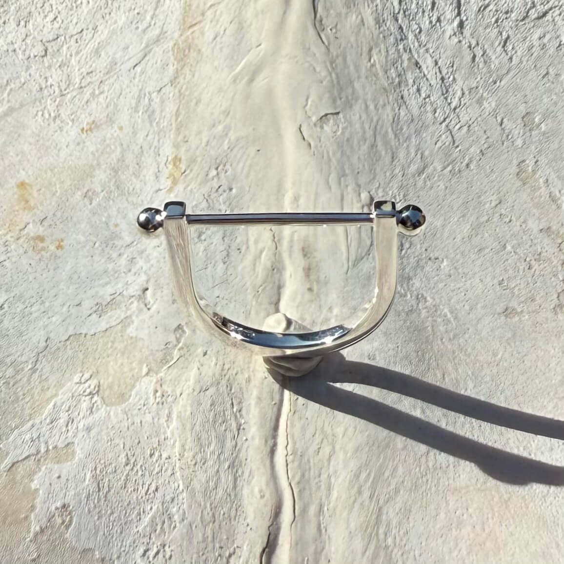 Metallic U-shaped silver bar stackable ring on a textured stone surface