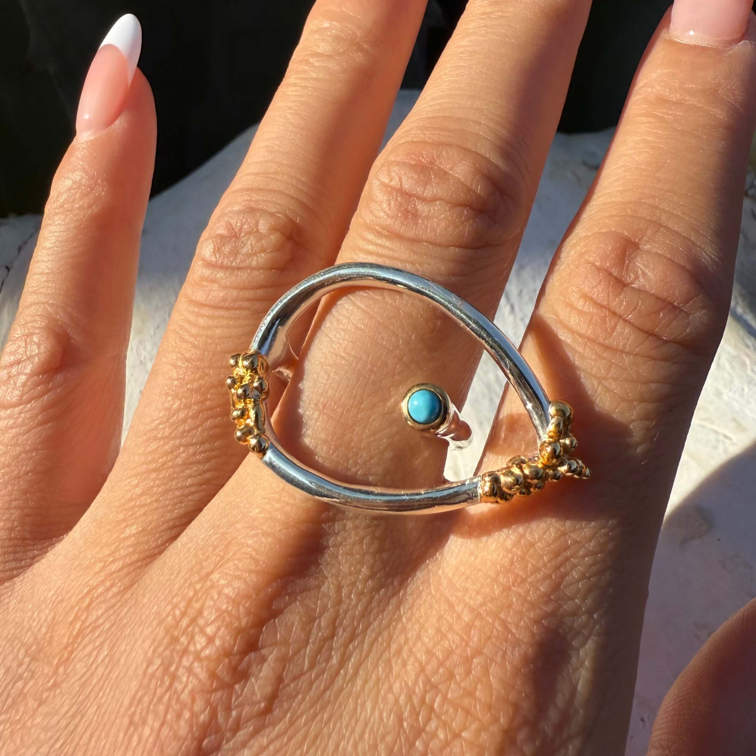 Close-up of a hand wearing a silver and gold ring with a turquoise stone.
