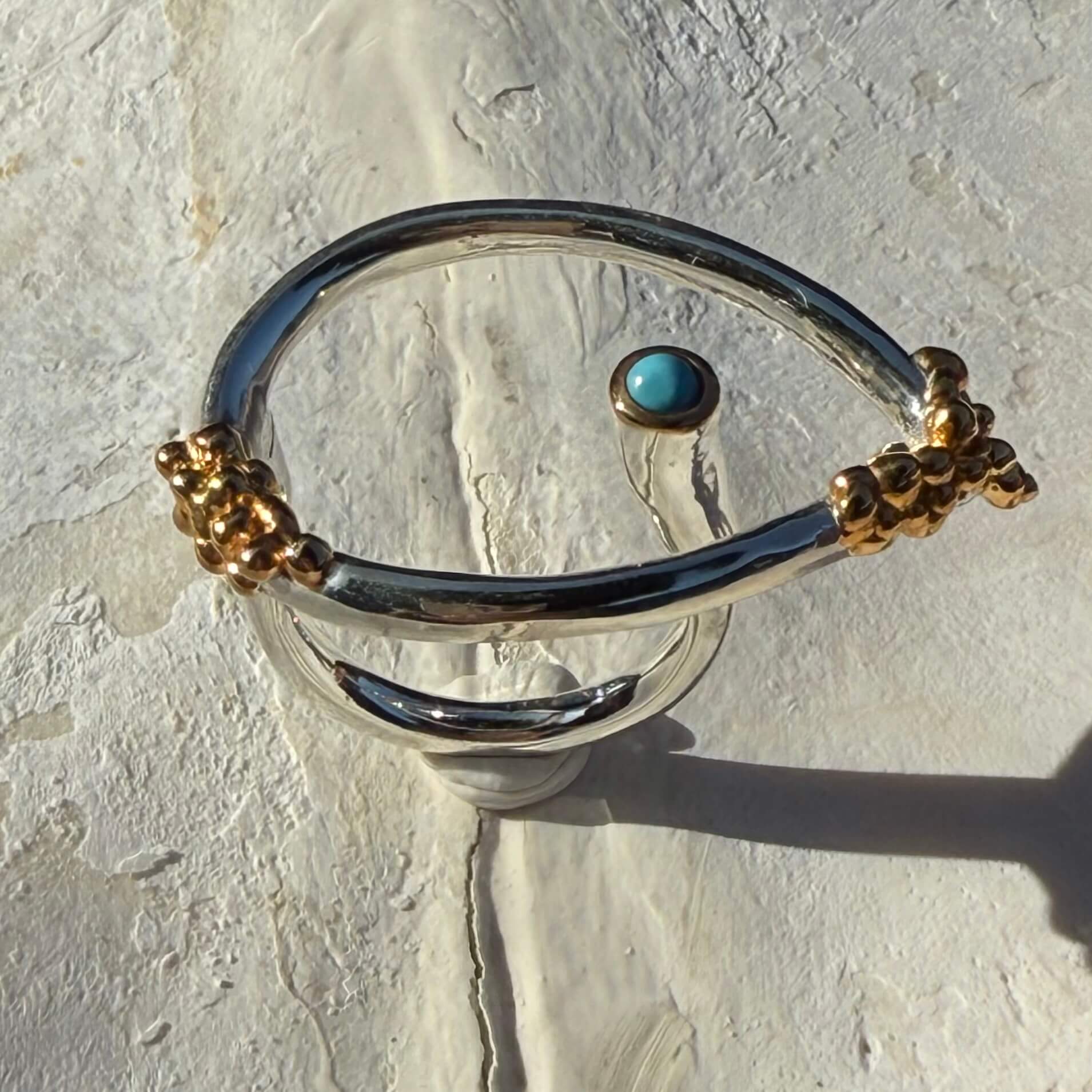 Silver bangle with gold accents and a turquoise stone on a textured white surface