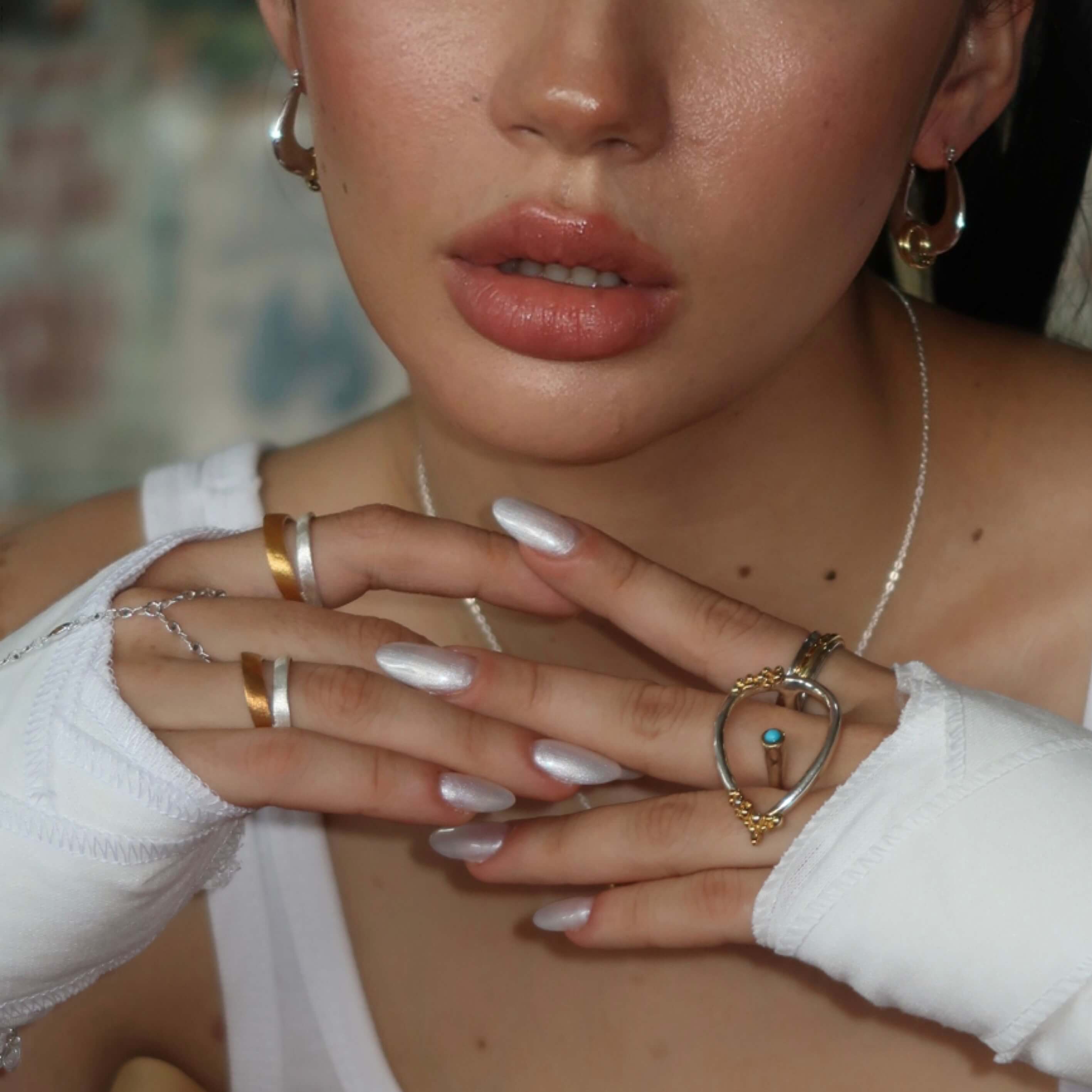Close-up of a person's hand with multiple rings and white gloves, wearing gold hoop earrings.