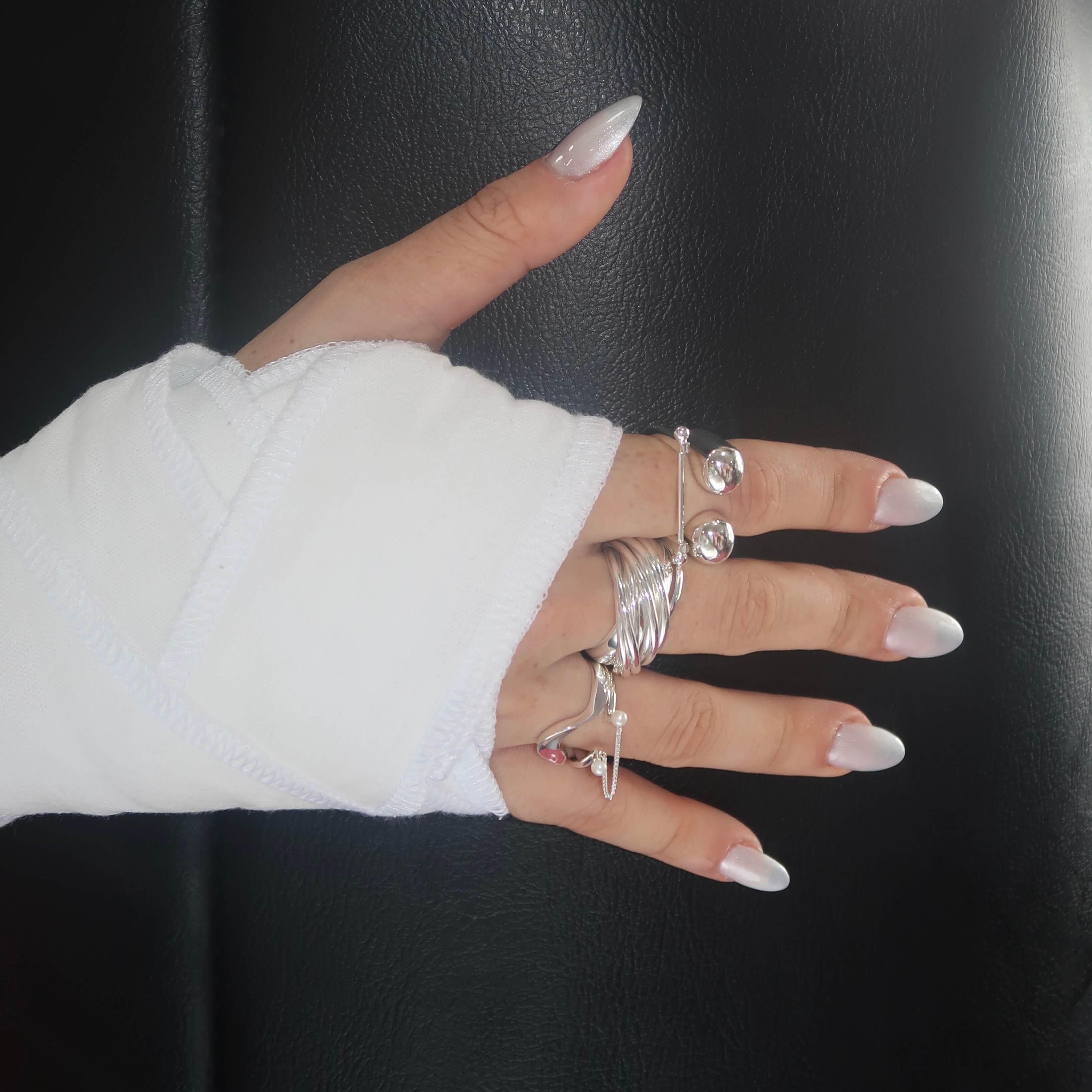Hand wearing multiple silver rings with a white sleeve against a dark background