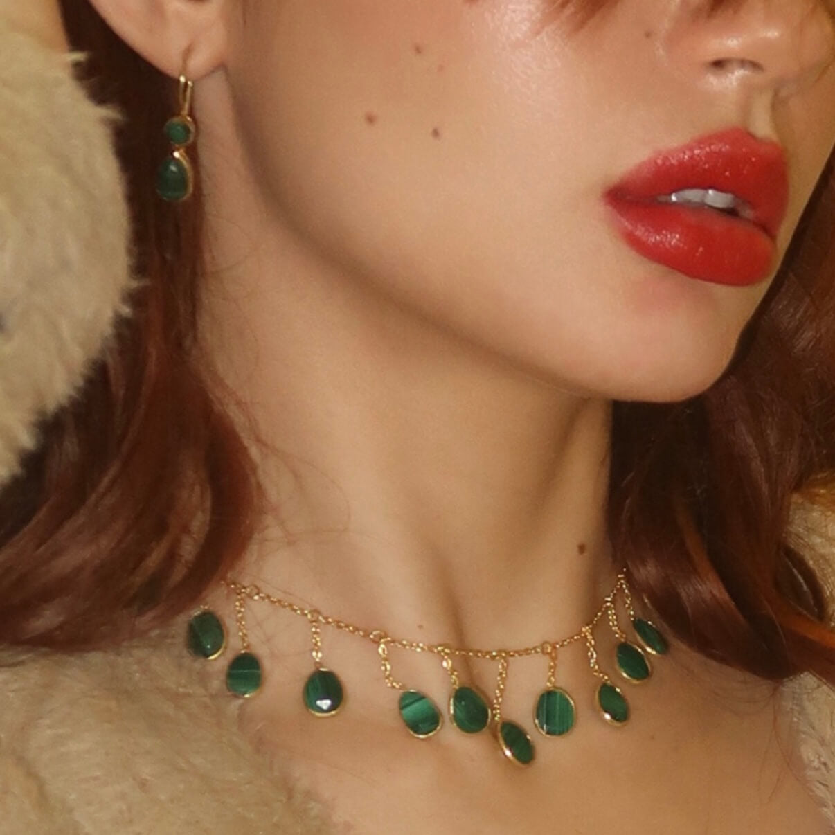 Close-up of a person wearing a gold necklace with green malachite gemstones and earrings.