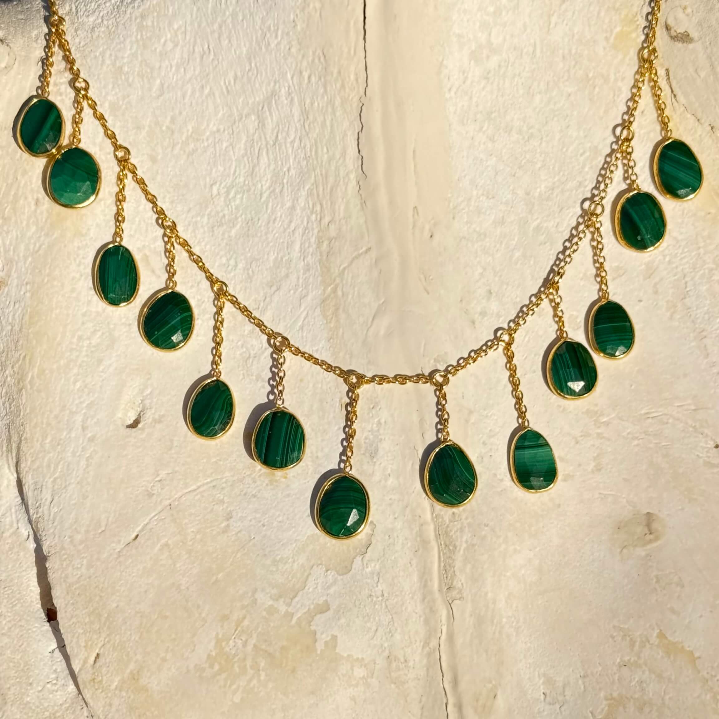 Gold necklace with green malachite stones on a textured beige surface