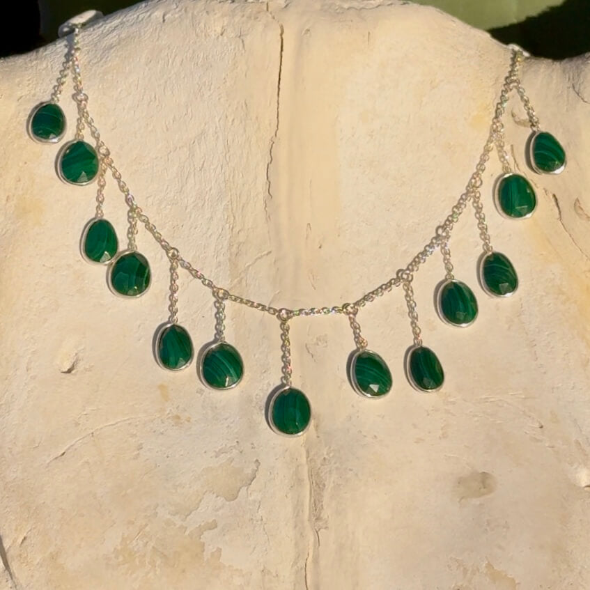 Silver necklace with green malachite stones on a stone surface