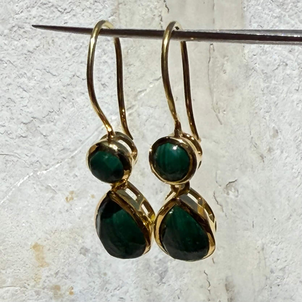 Gold earrings with green gemstones on a textured white background