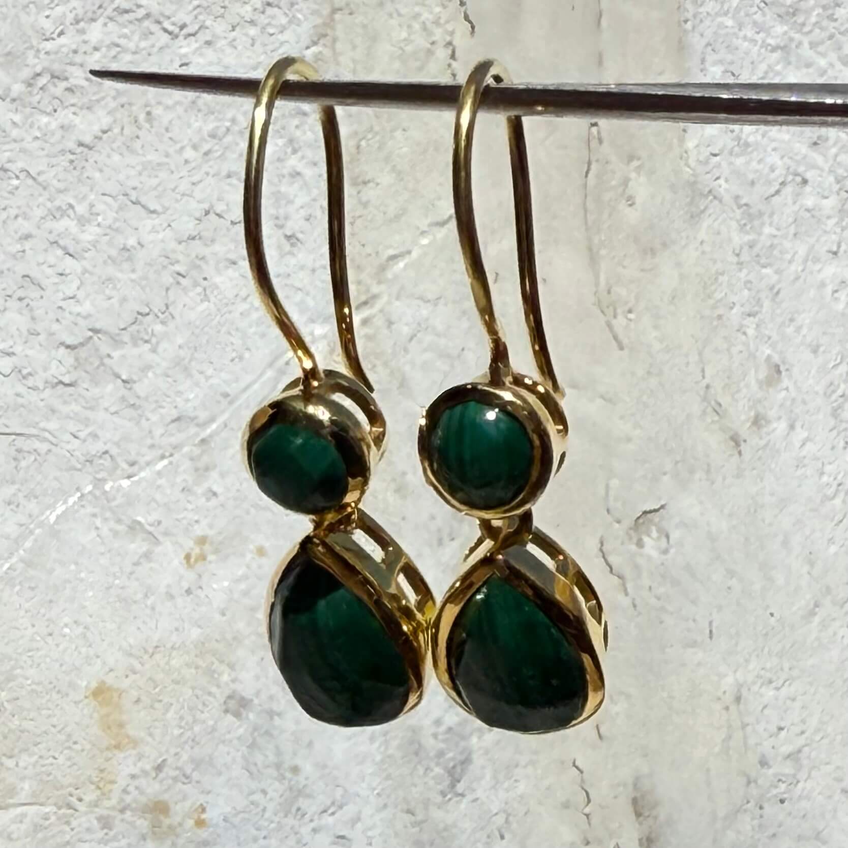 Gold earrings with green gemstones on a textured white background