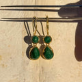 Gold earrings with green gemstones on a textured beige surface