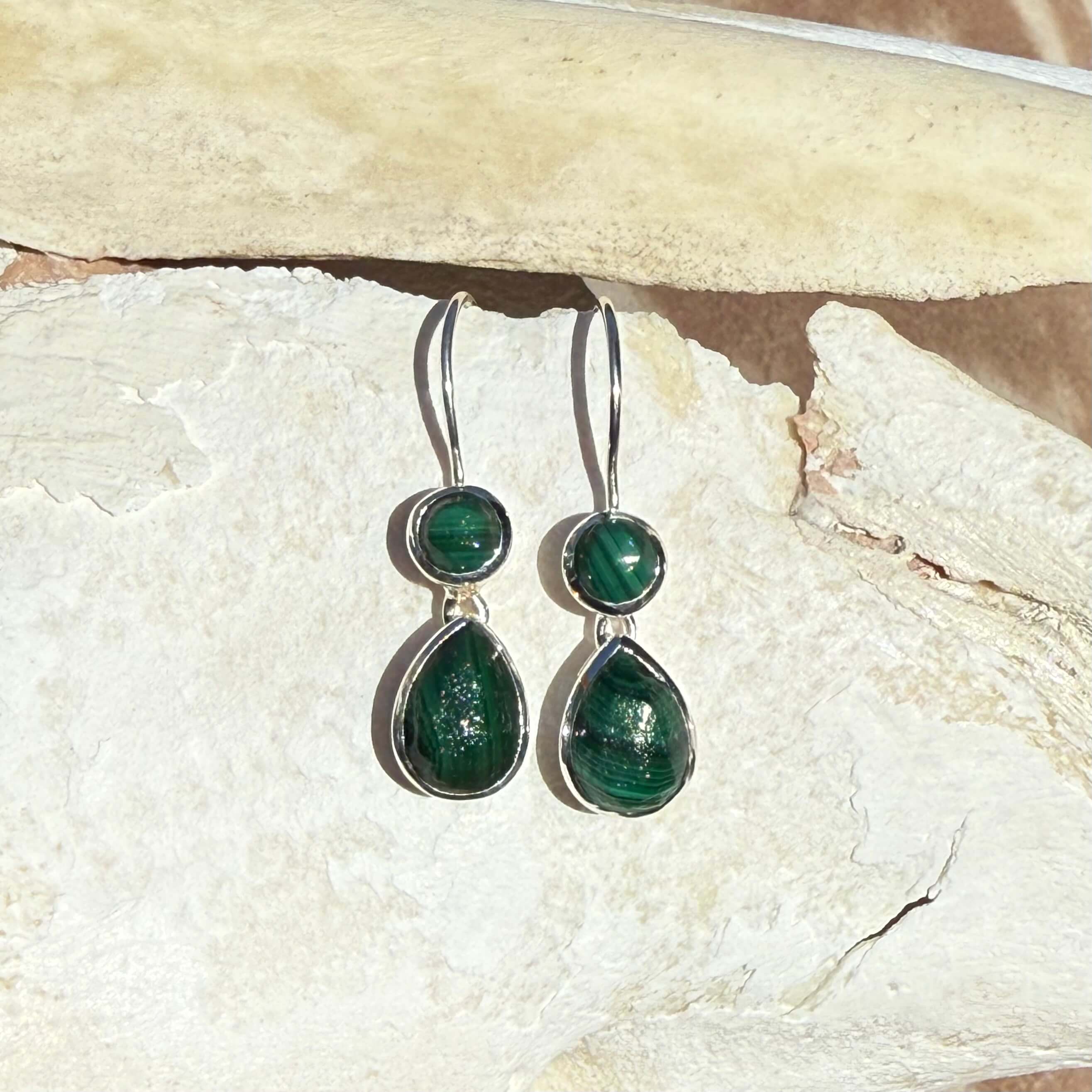 Pair of green teardrop earrings on a textured stone surface