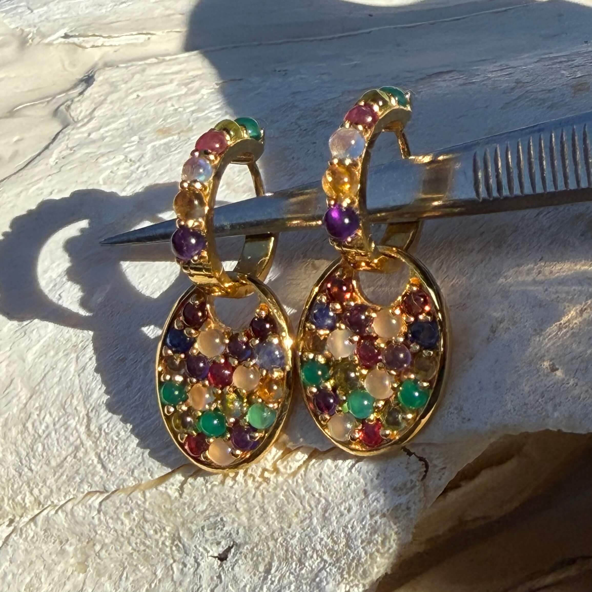 Gold earrings with colorful gemstones on a textured surface