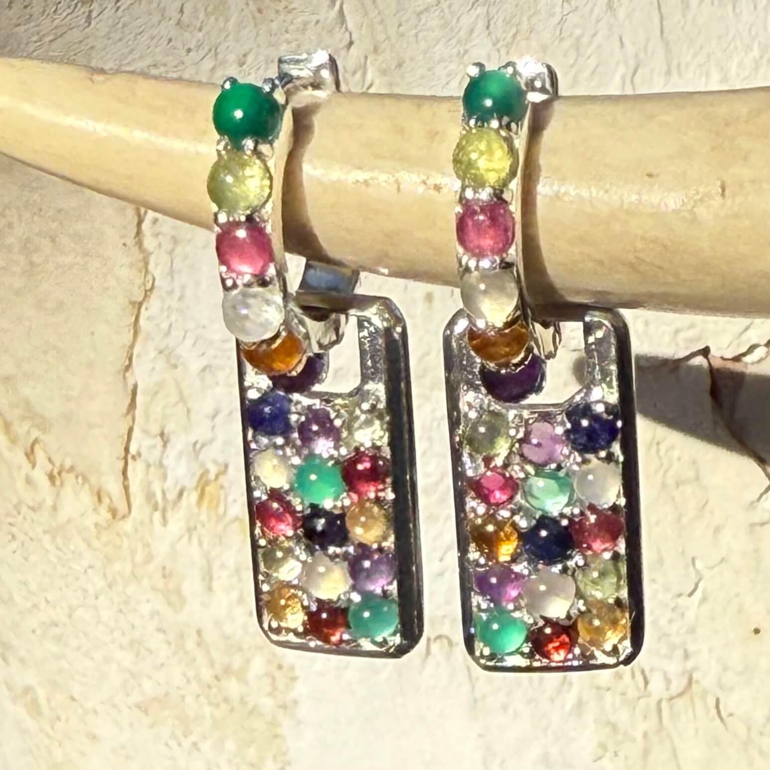 Multicolored gemstone earrings on a wooden stick against a beige background