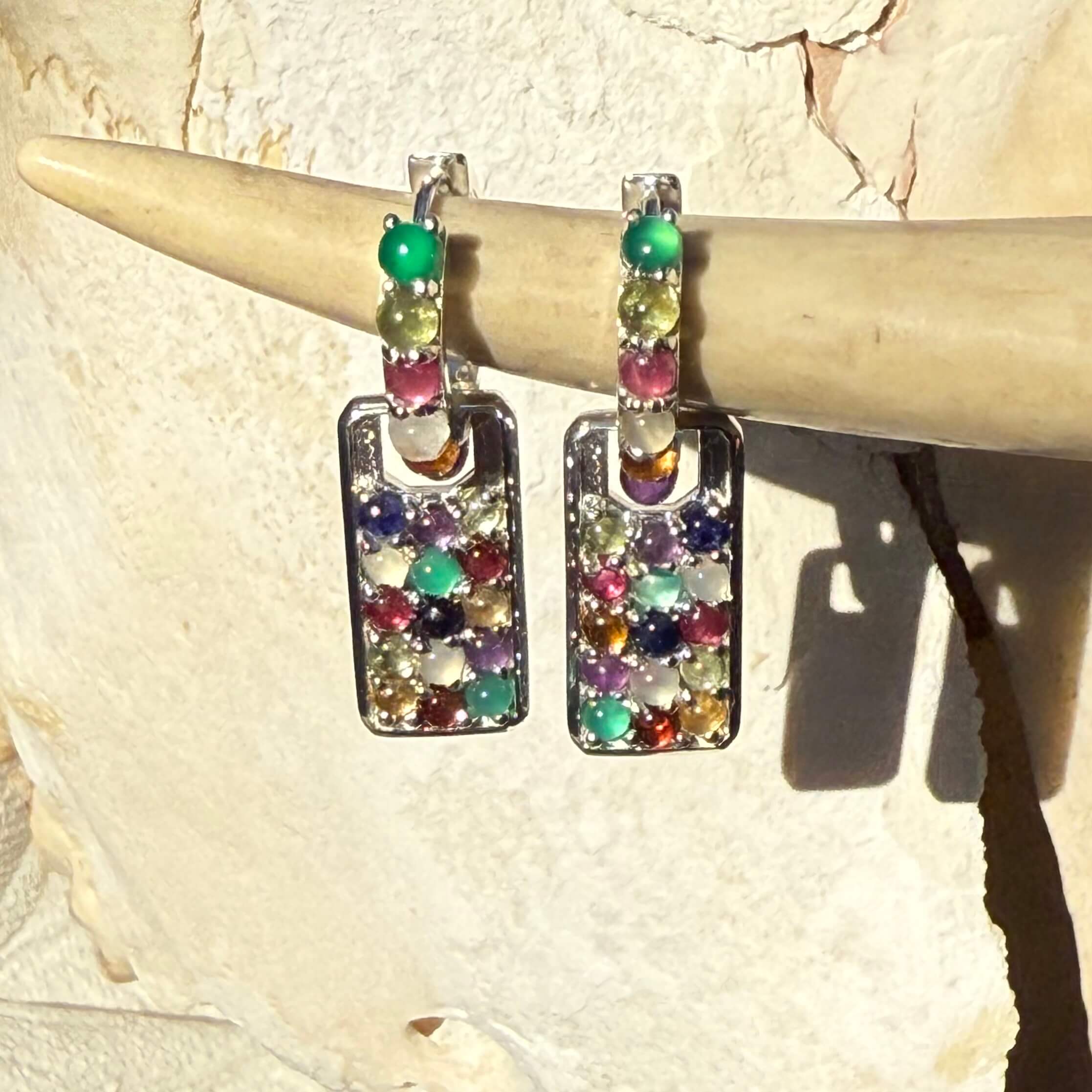 Multicolored gemstone on silver earrings on a stone surface