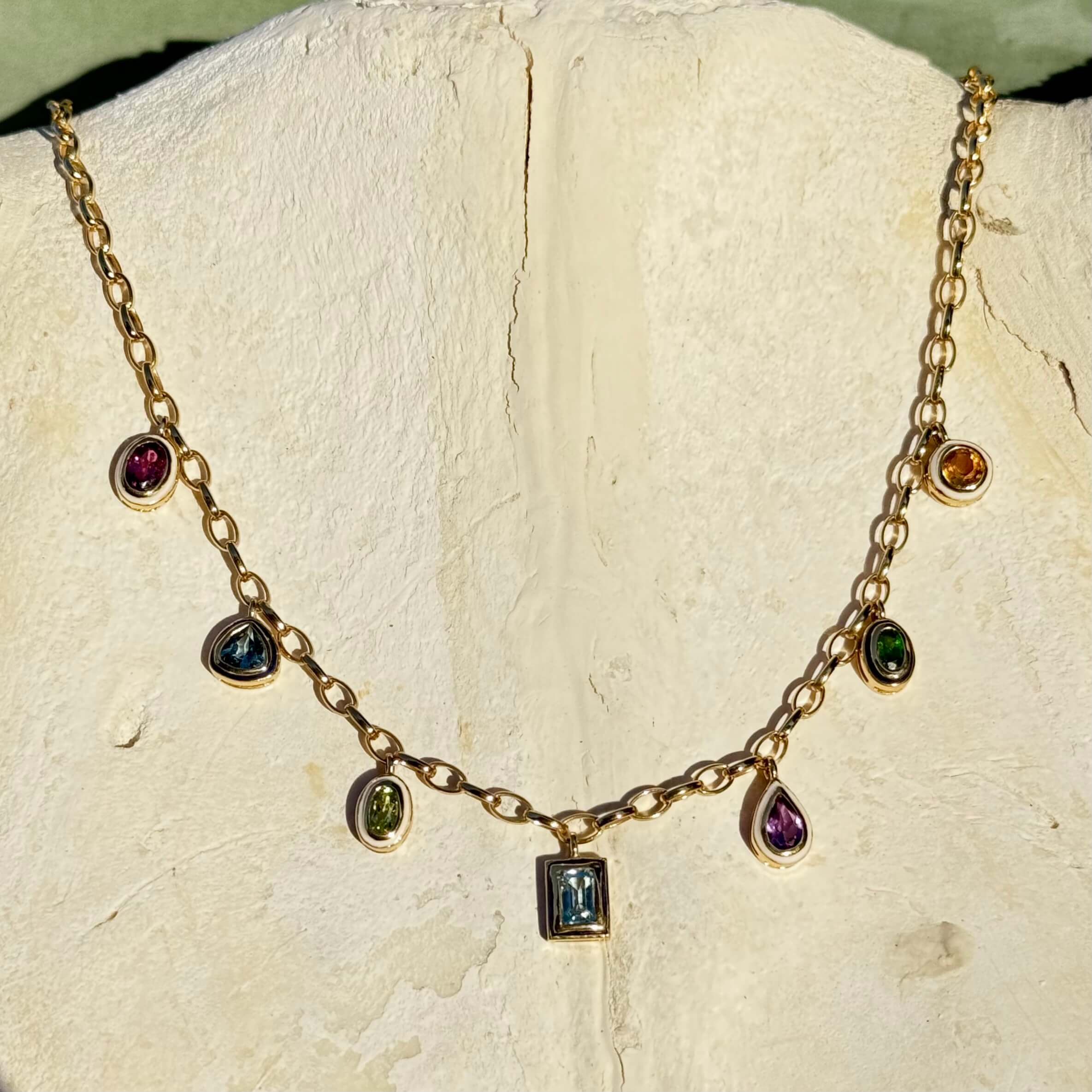 Gold necklace with gemstones on a textured white surface