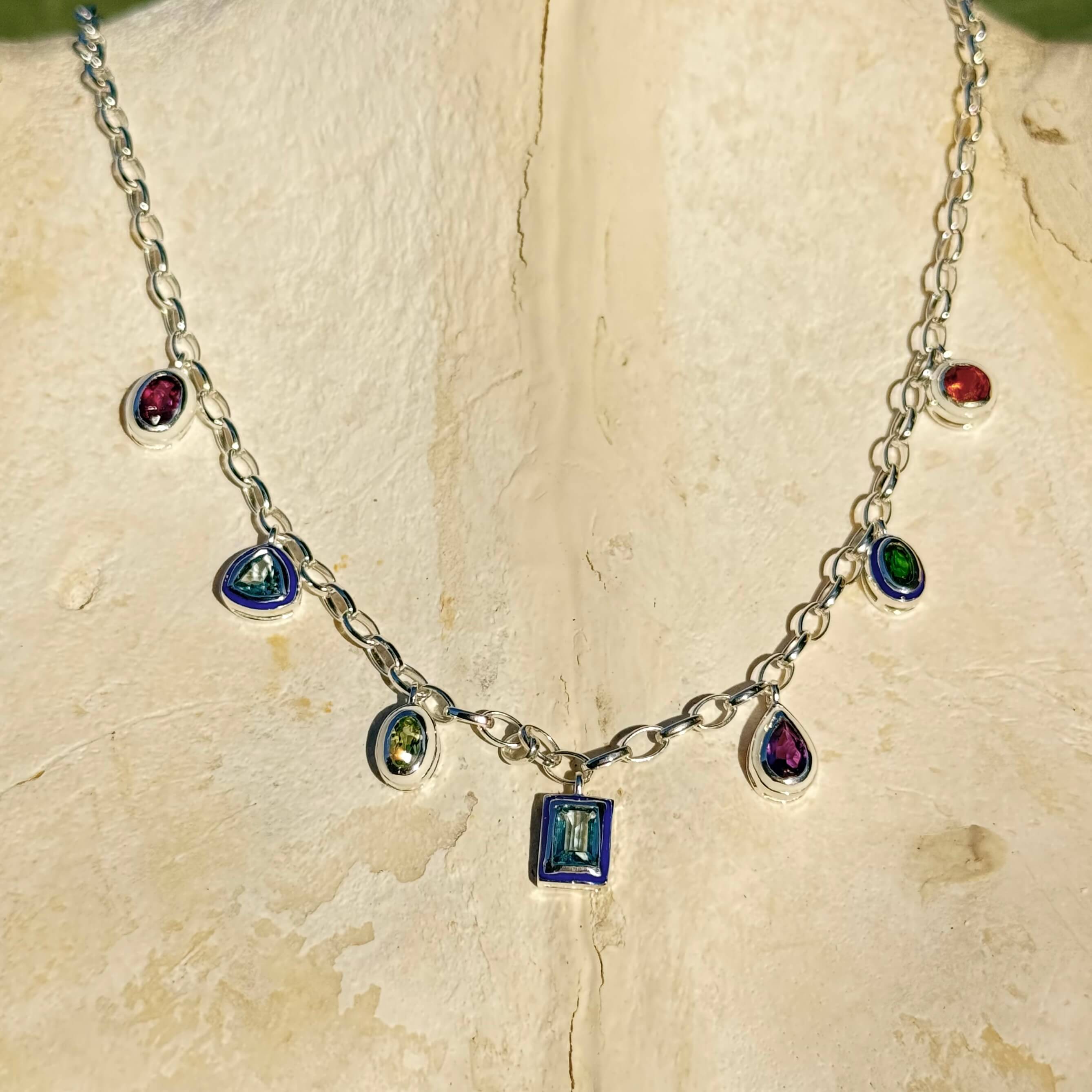 Silver necklace with colorful gemstones on a textured beige surface