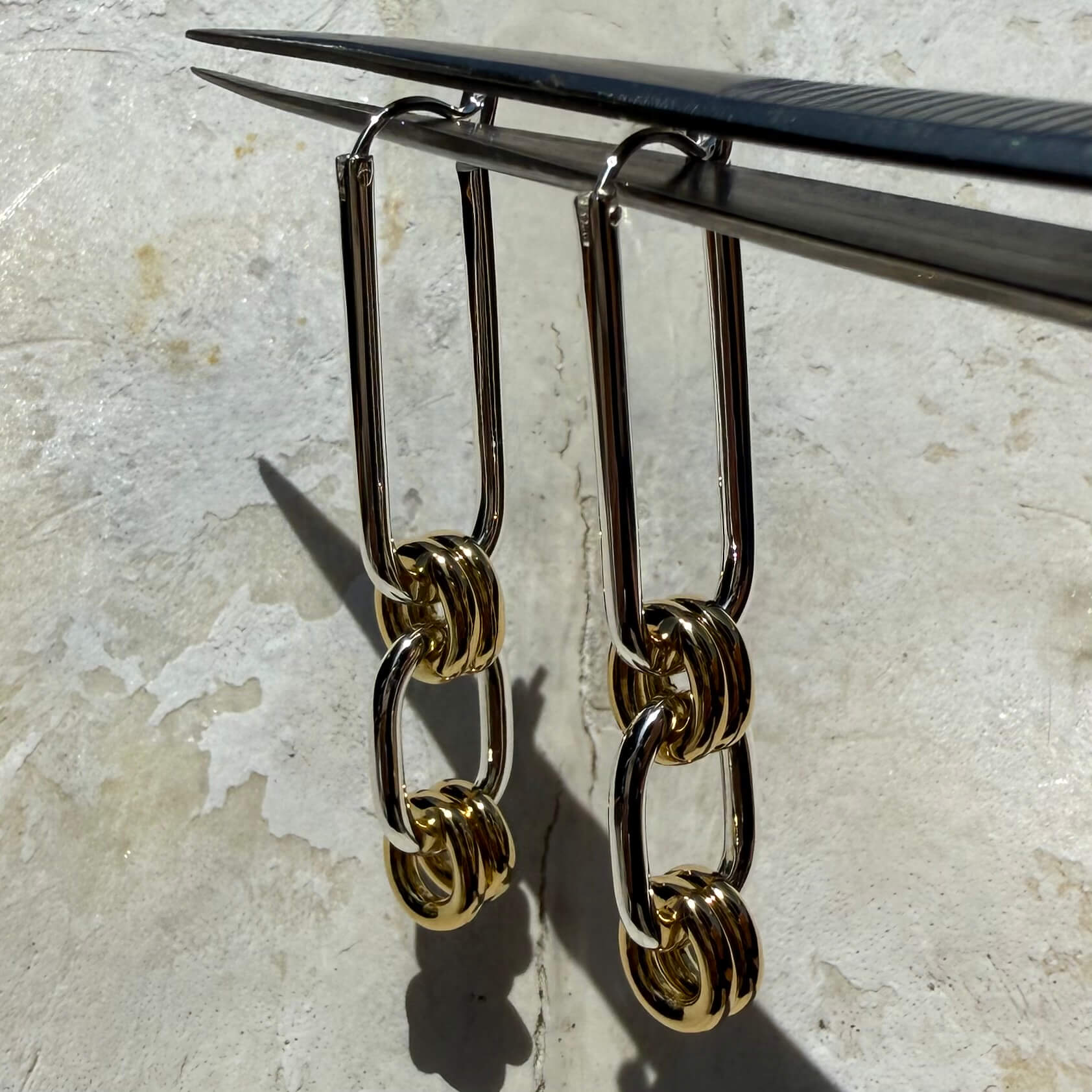 Gold chain-style earrings on a metallic stand against a textured surface