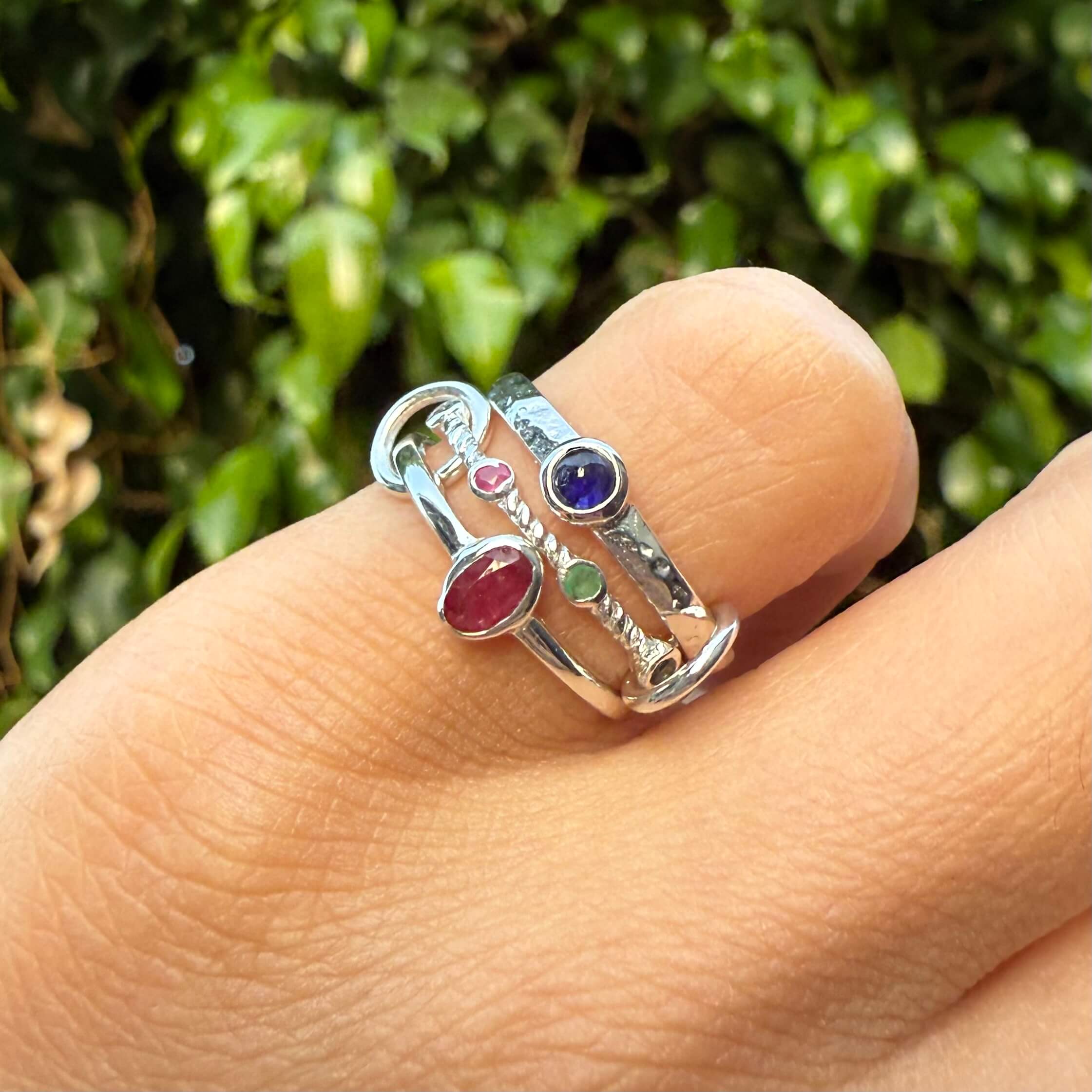 Three silver rings with gemstones on a finger against a green leafy background