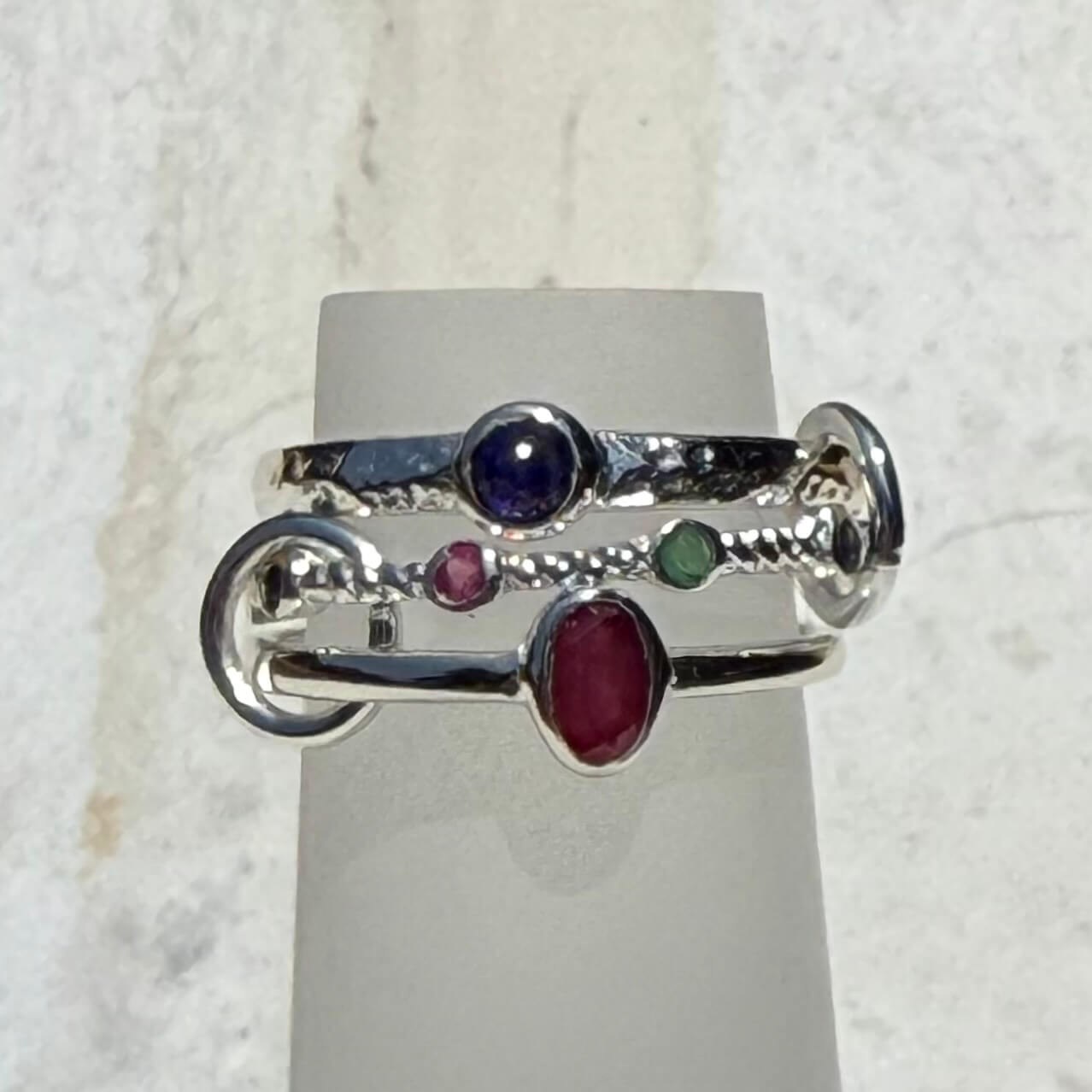 Silver ring with colored gemstones on a gray stand against a light background