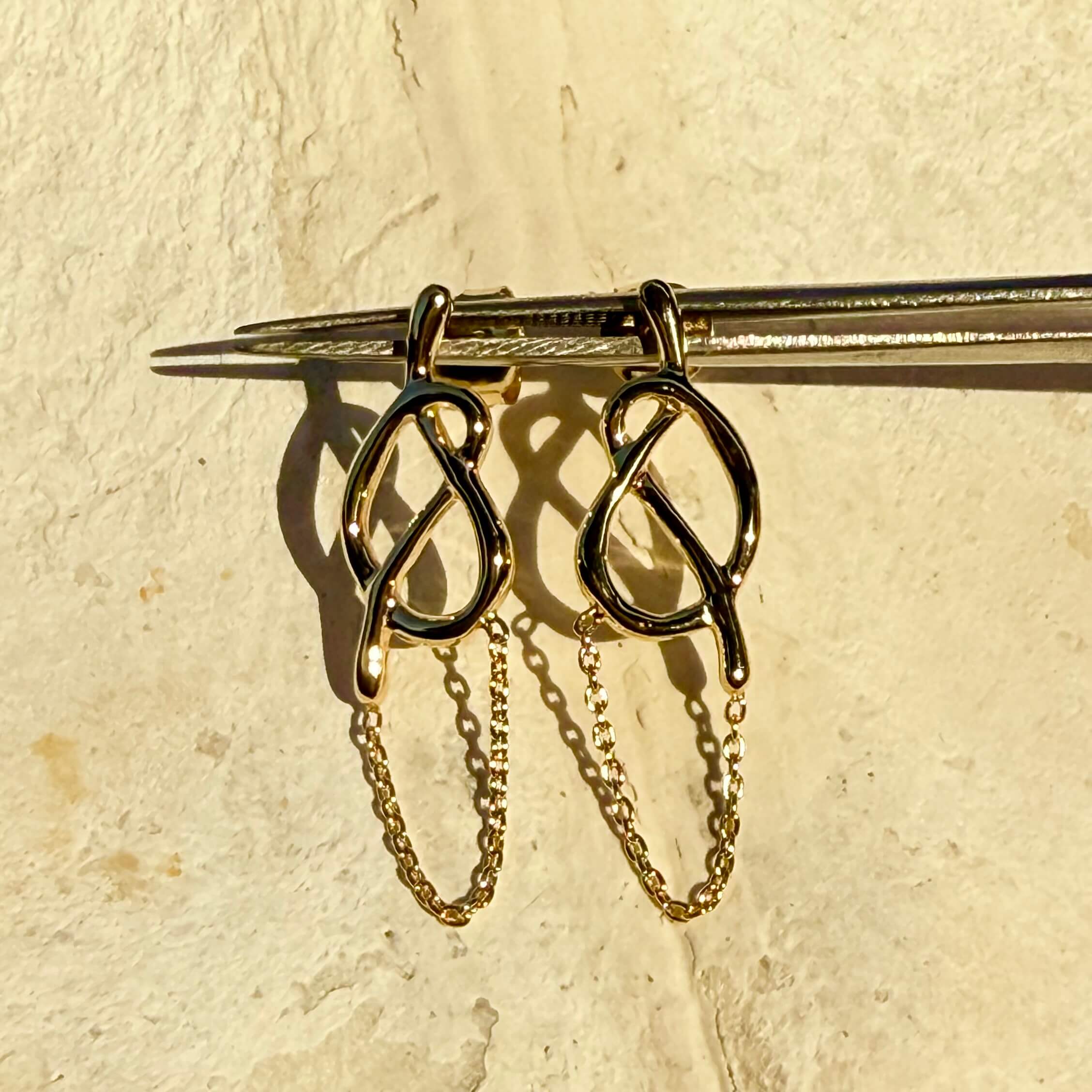 Gold earrings with chain details on a beige background