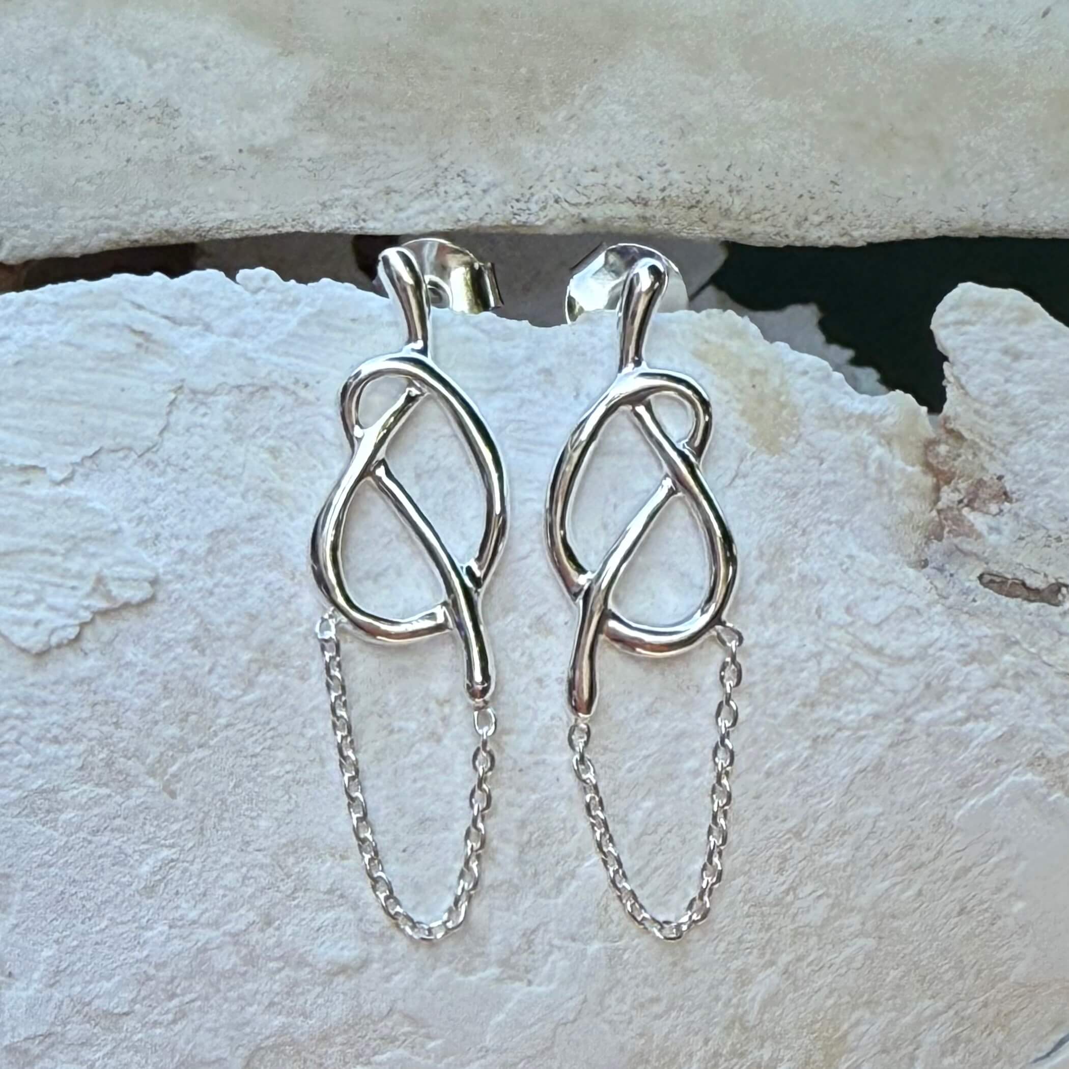 Silver earrings with chain details on a textured stone surface
