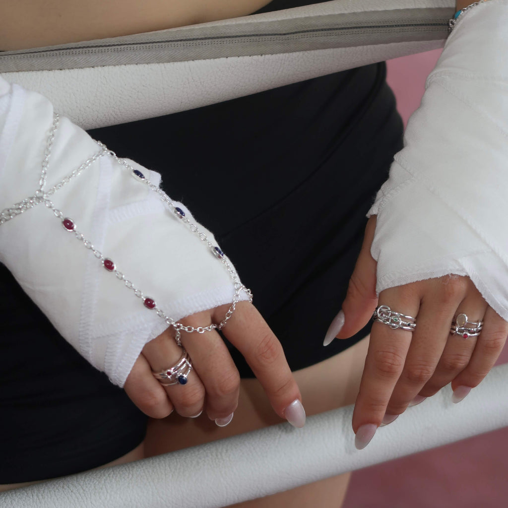 Close-up of hands with multiple rings and bracelets on a white surface