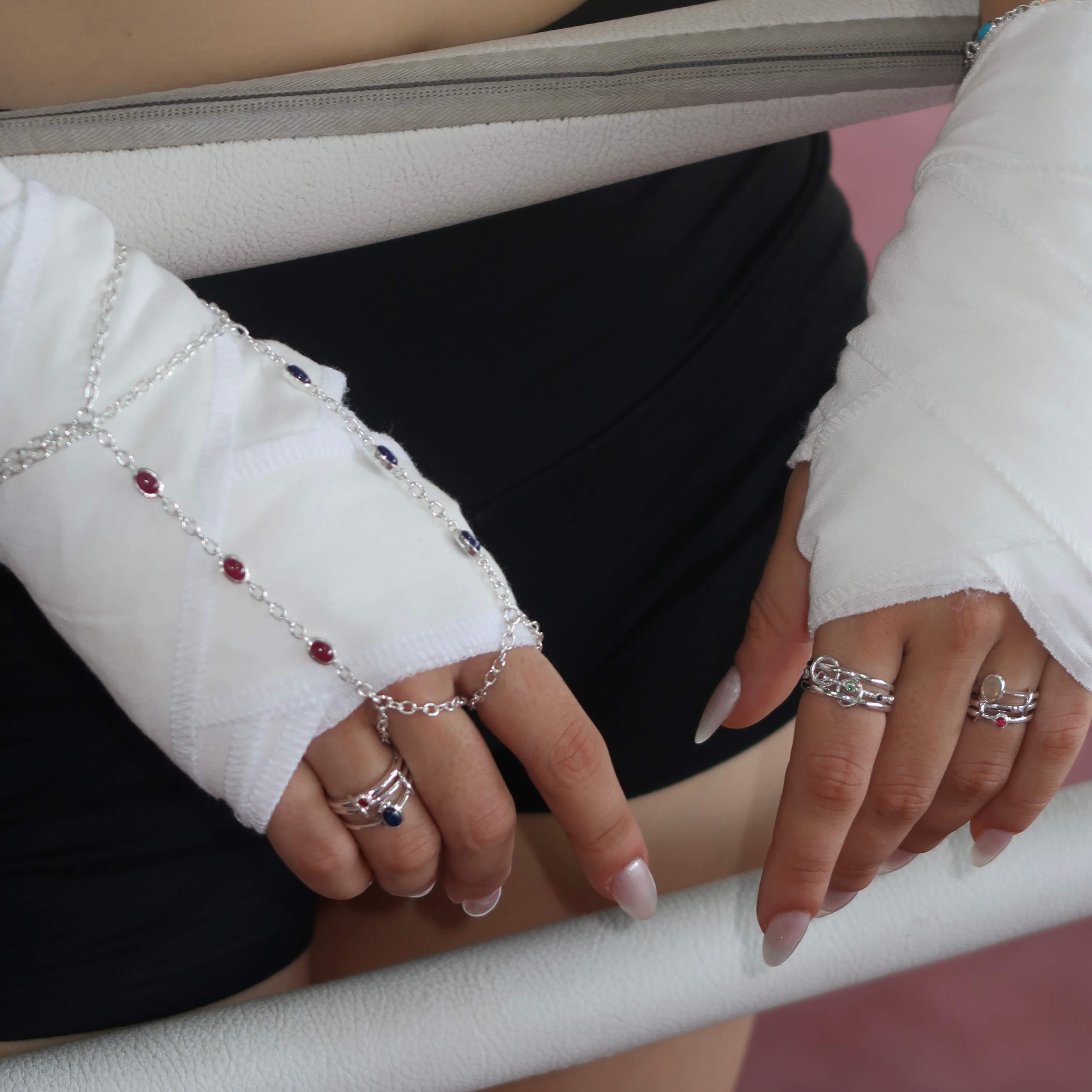 Close-up of hands with multiple rings and bracelets on a white surface