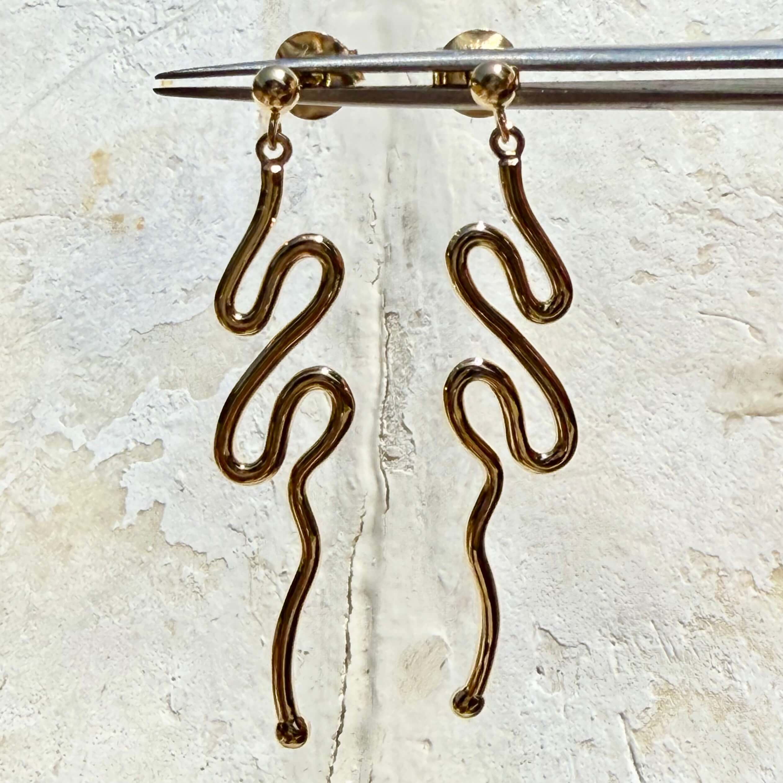 Gold snake-shaped earrings on a textured beige background