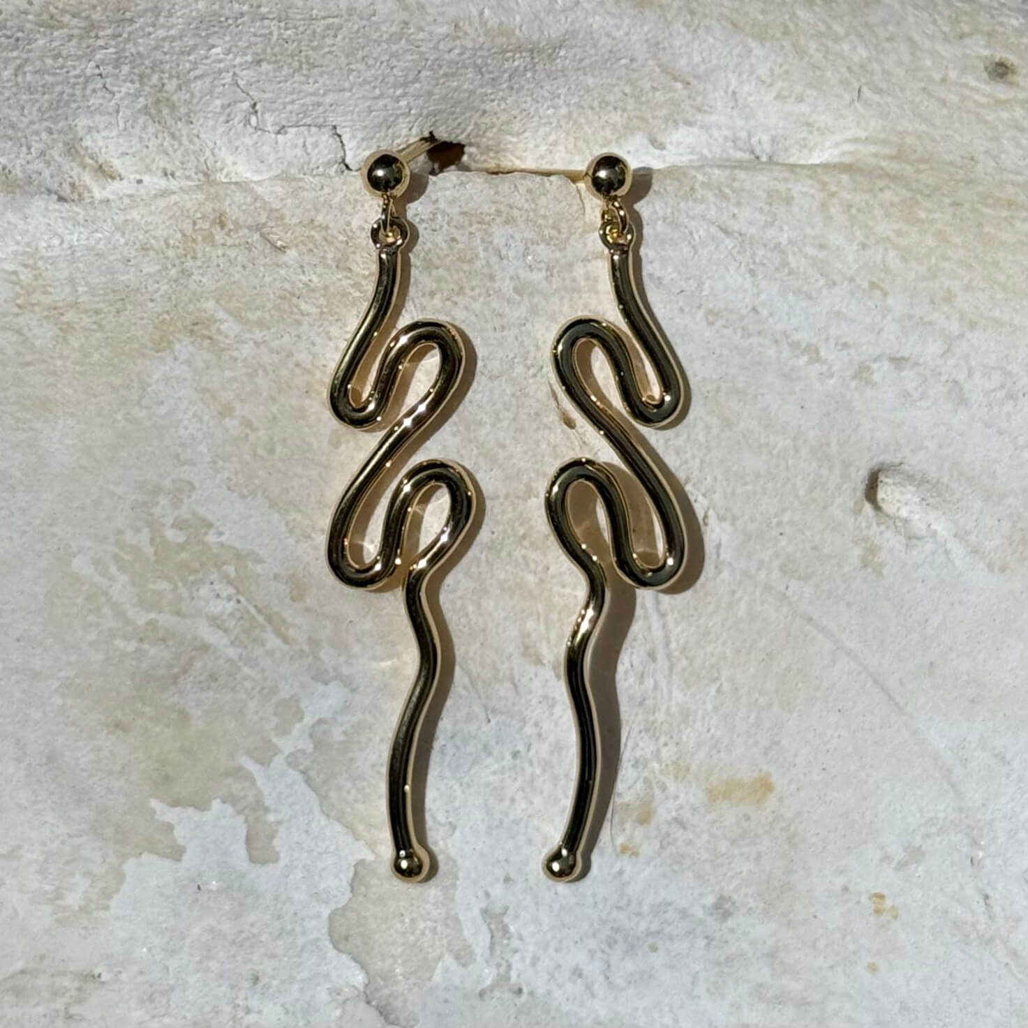 Gold snake-shaped earrings on a light stone background