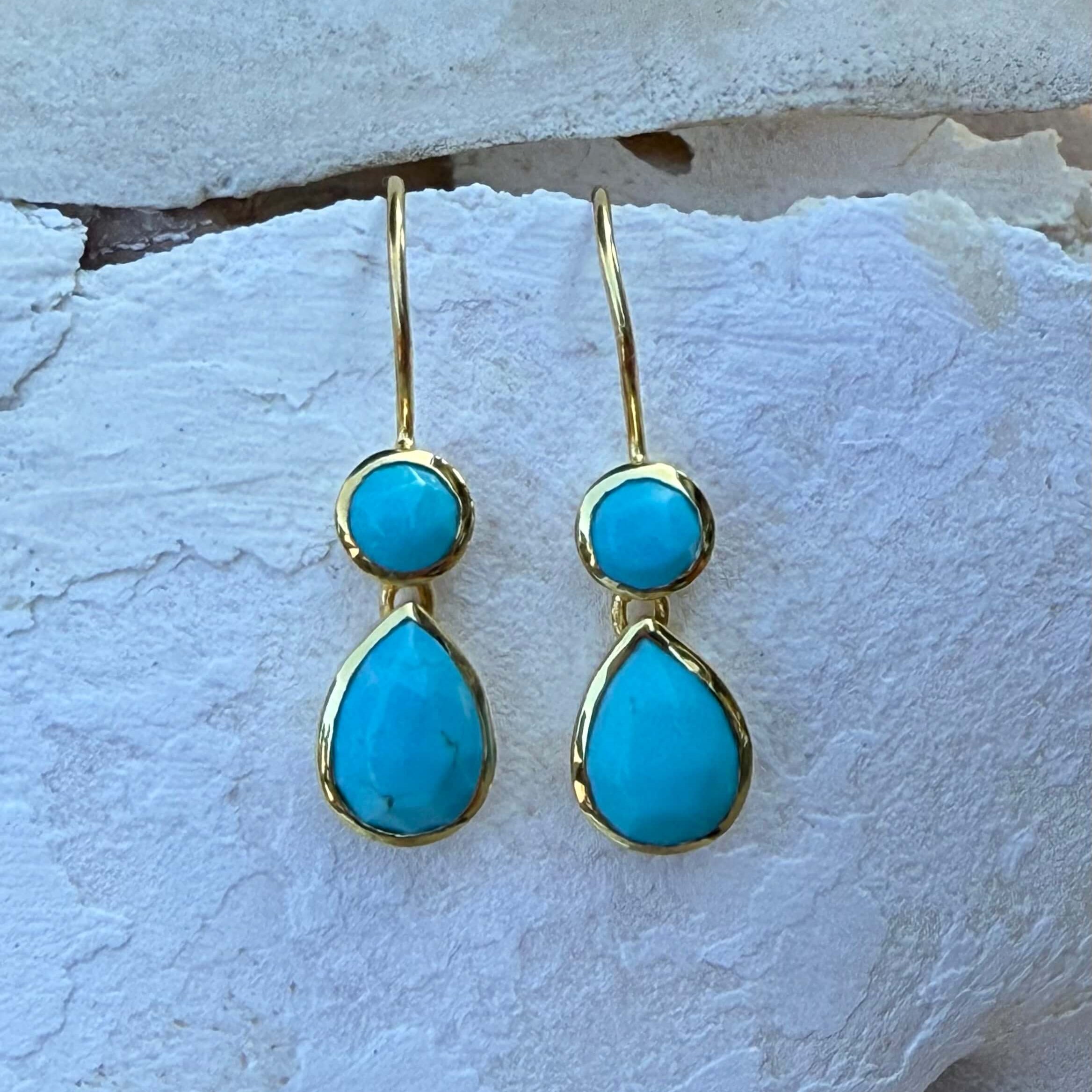 Turquoise teardrop earrings with gold accents on a textured white surface