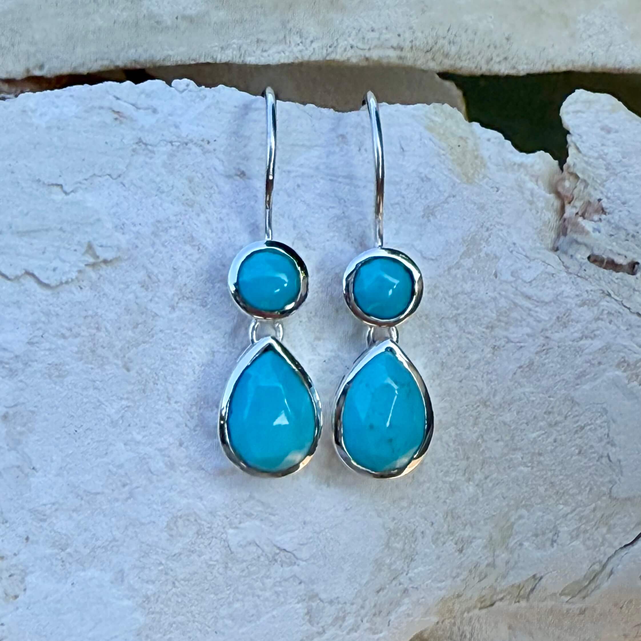 Turquoise teardrop silver earrings on a textured stone surface