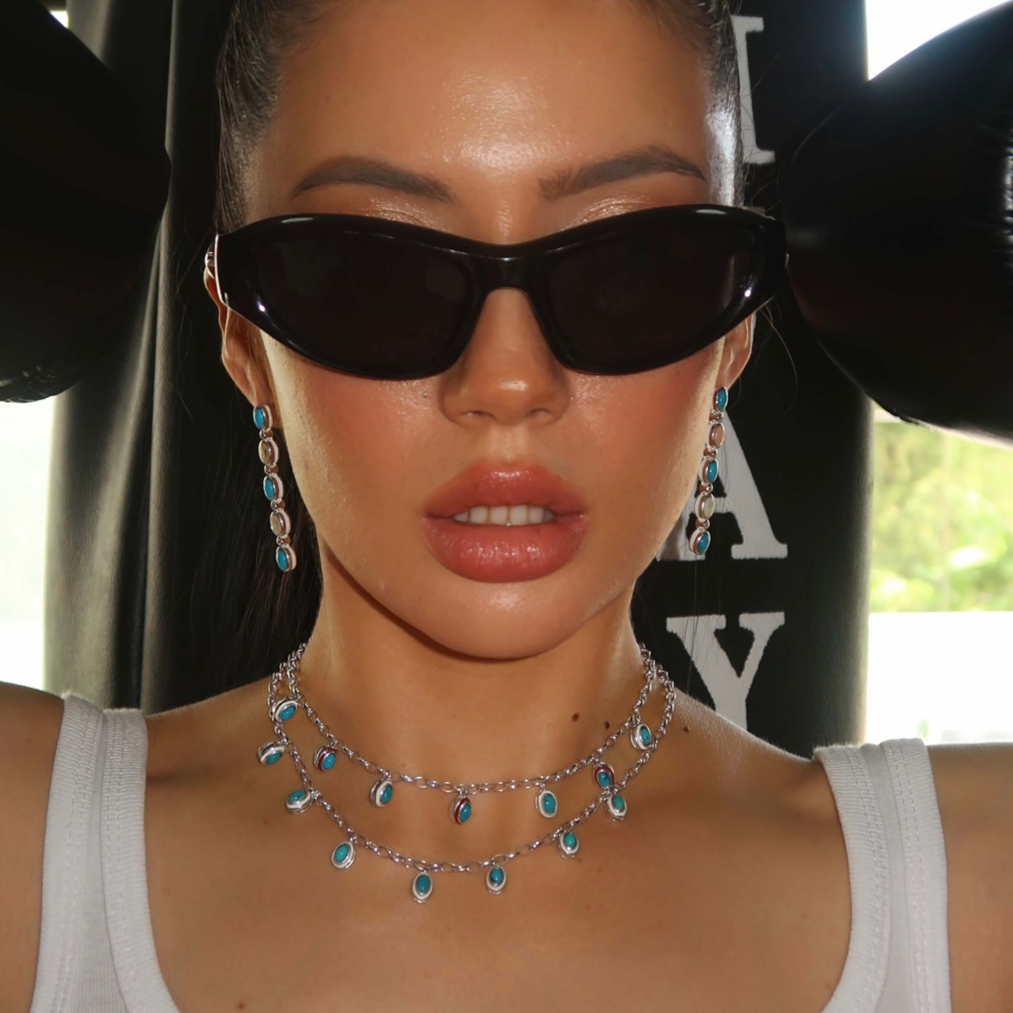 Person wearing turquoise necklace with sunglasses and a white top