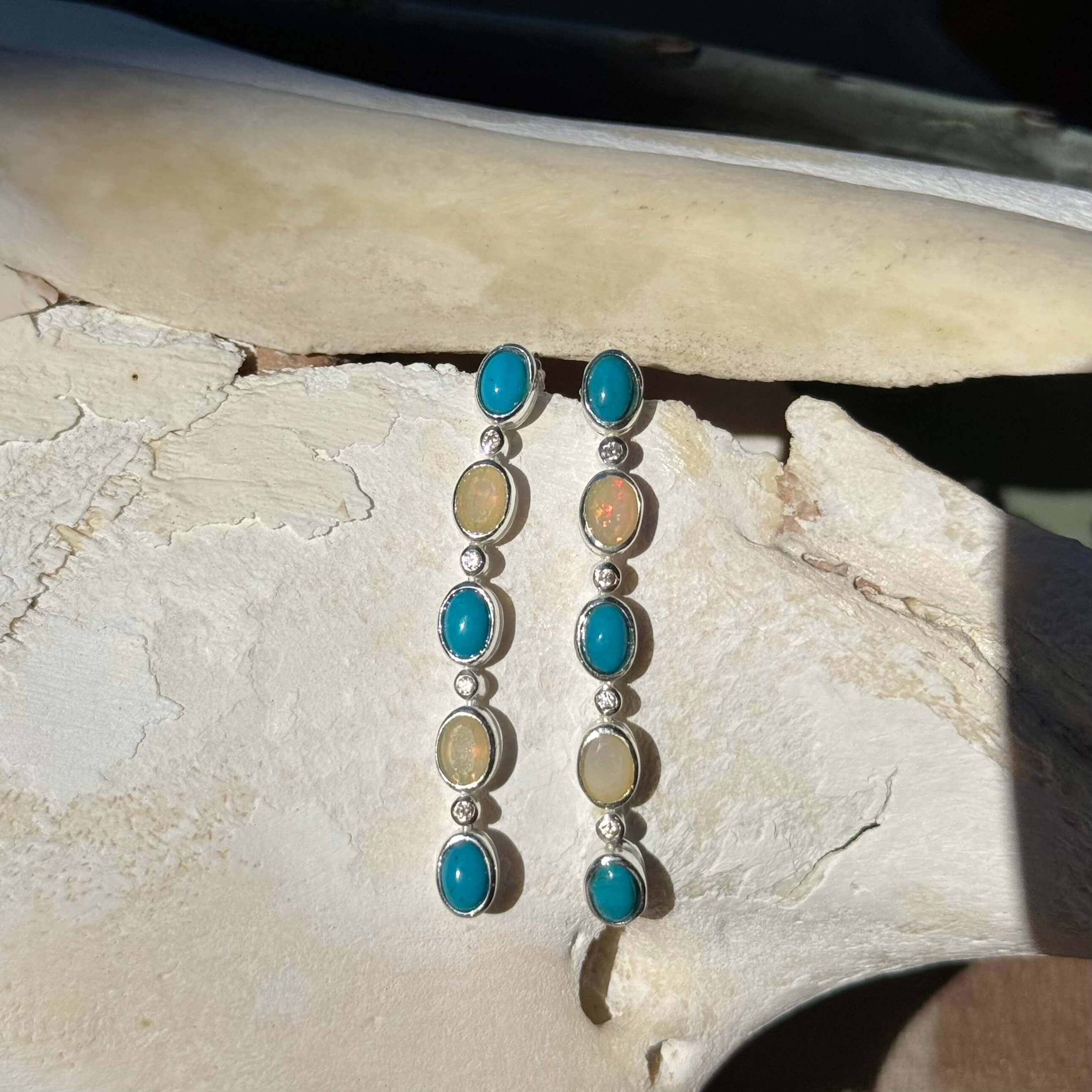 Pair of earrings with turquoise and opal stones on a stone surface