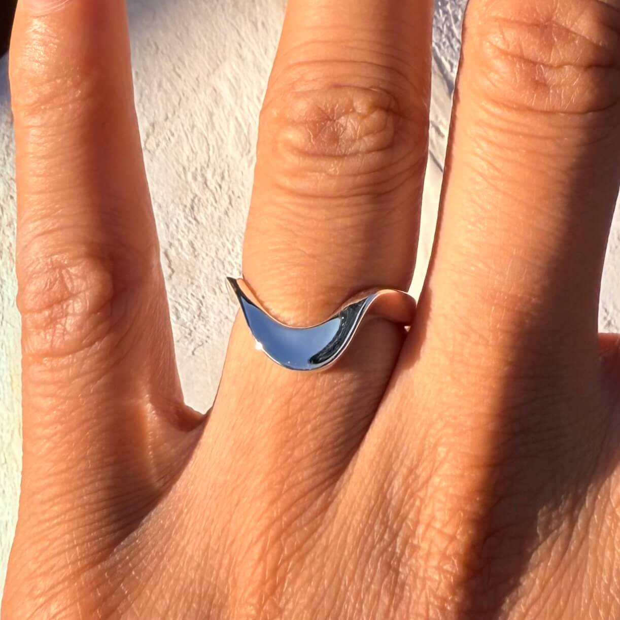 Wavy stackable silver ring on a person's finger against a neutral background