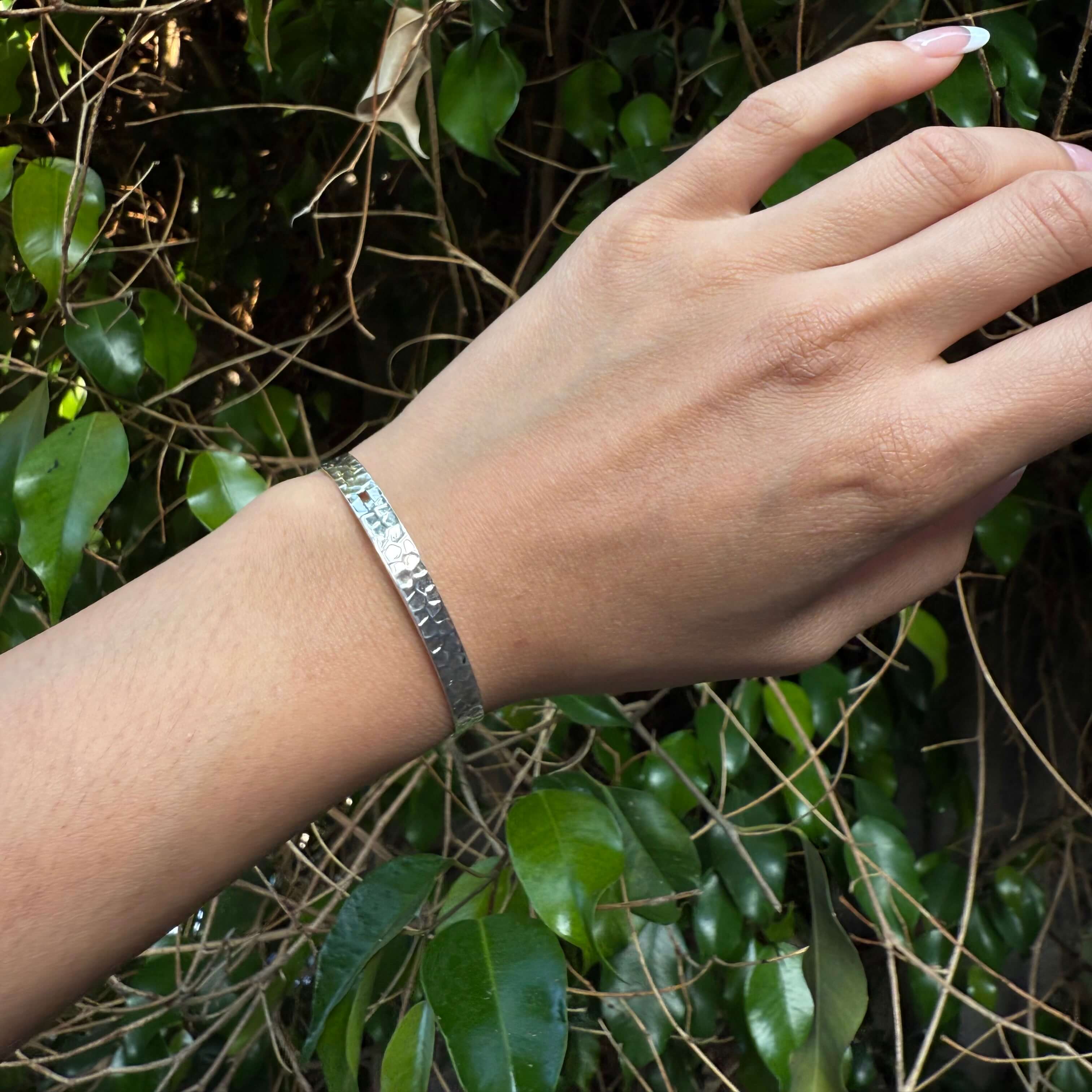 Hand wearing a silver bracelet with a green leafy background